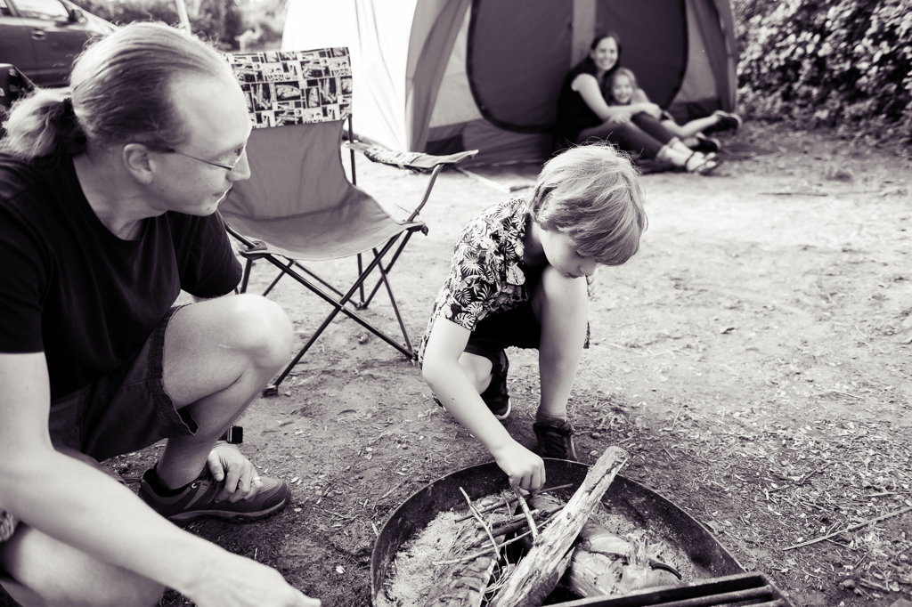 a young boy learns how to start a campfire by his dad