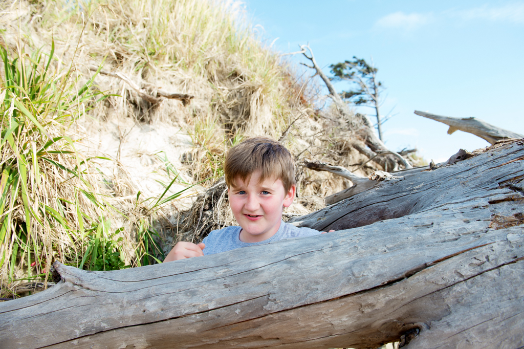 a young boy peeks from behind driftwood at cape lookout