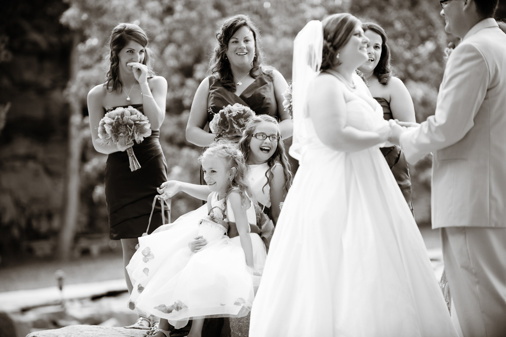 bridesmaids and flower girls stand behind bride during ceremony and laugh 