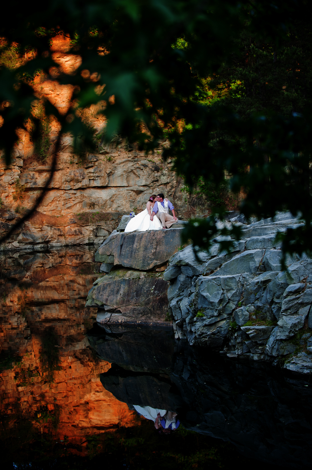 a bride and groom sit on the edge of a rock quarry
