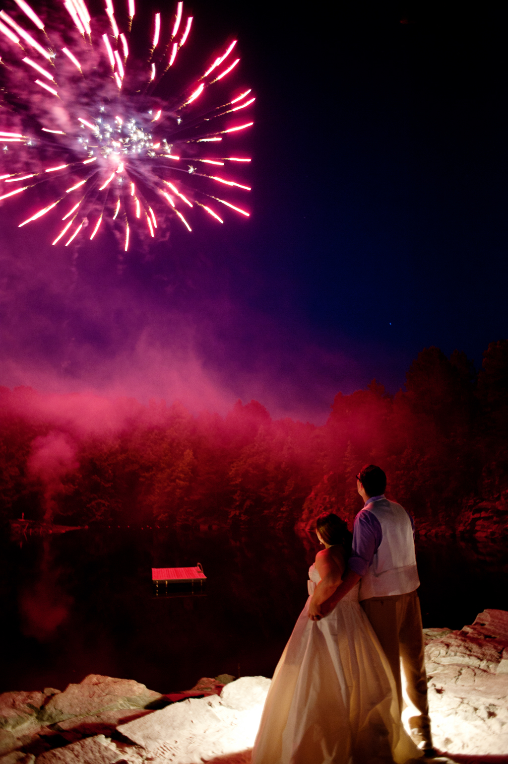 a bride and groom watch fireworks explode in the sky above a rock quarry