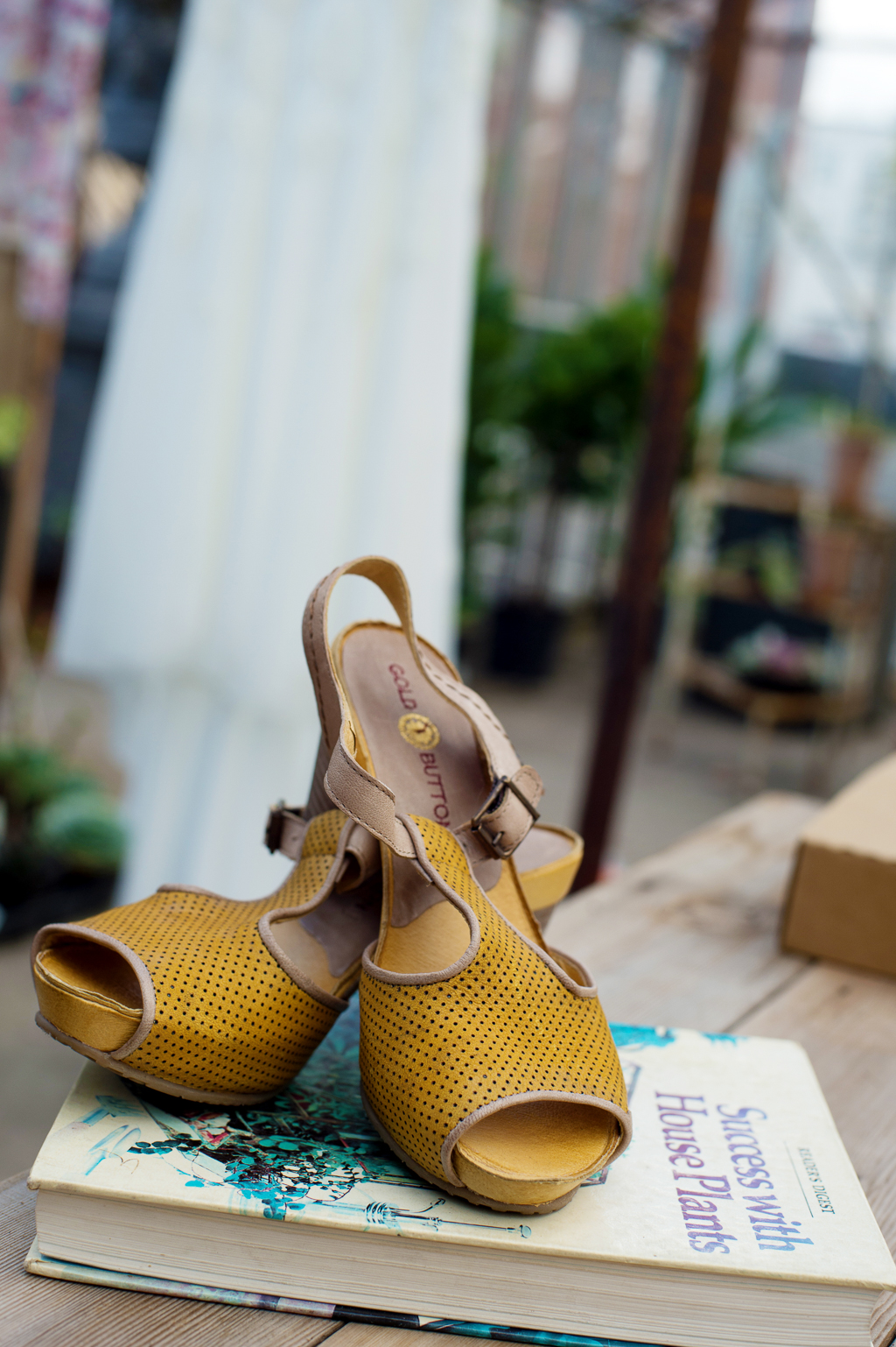 bride's vintage mustard yellow wedding shoes sit on a gardening book with her dress in the background