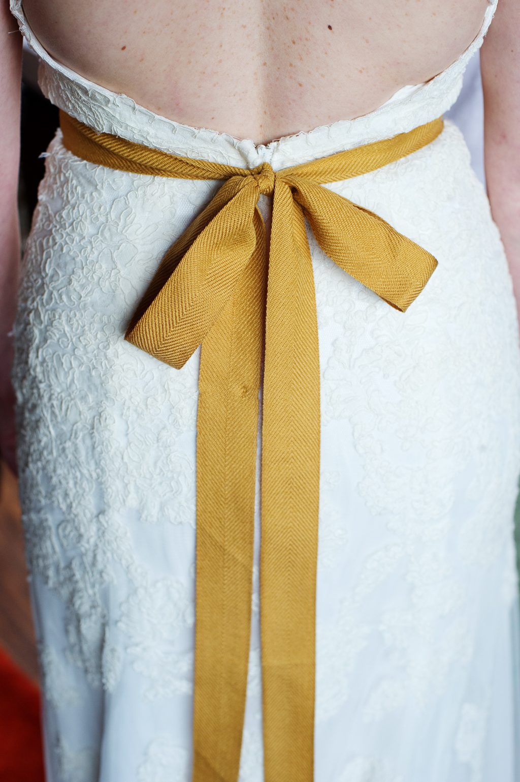 a mustard yellow ribbon is tied in a large bow around the back of a woman wearing a wedding dress