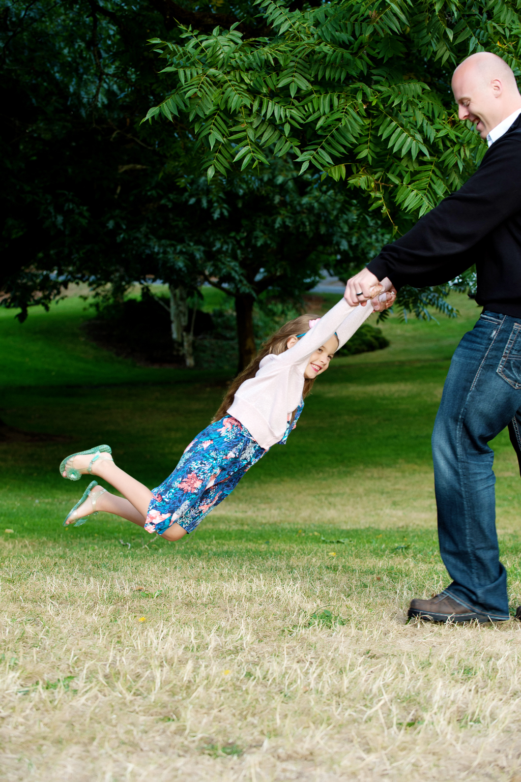 a dad holds a little girl by her hands and spins her around