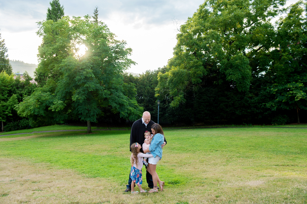 a family of four hug together as the sun shines through a tree at cathedral park