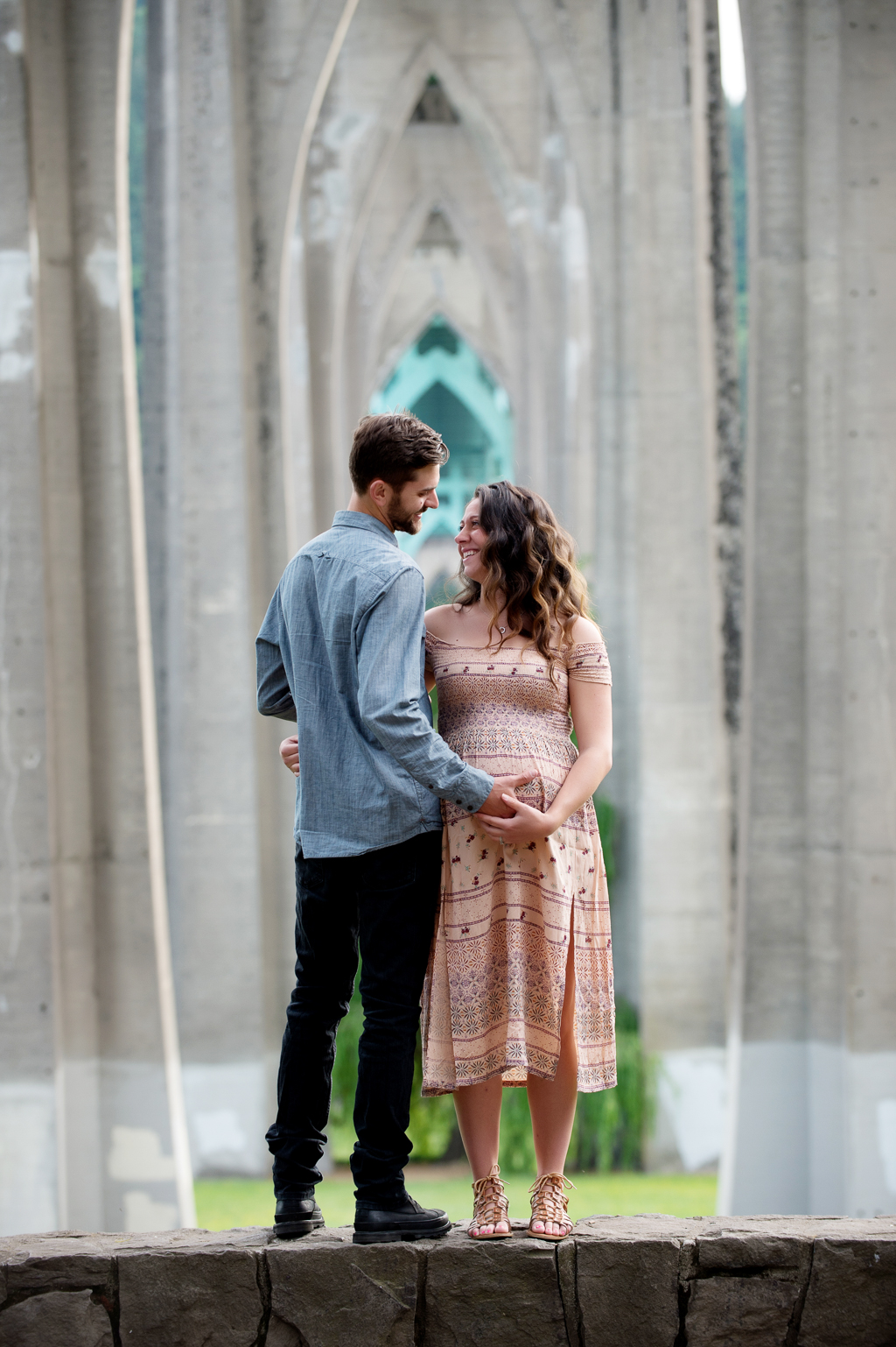 a pregnant woman and man holds her belly underneath the st johns bridge