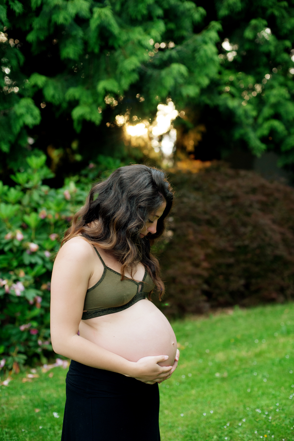 pregnant woman in forest green bralette  looks down at belly