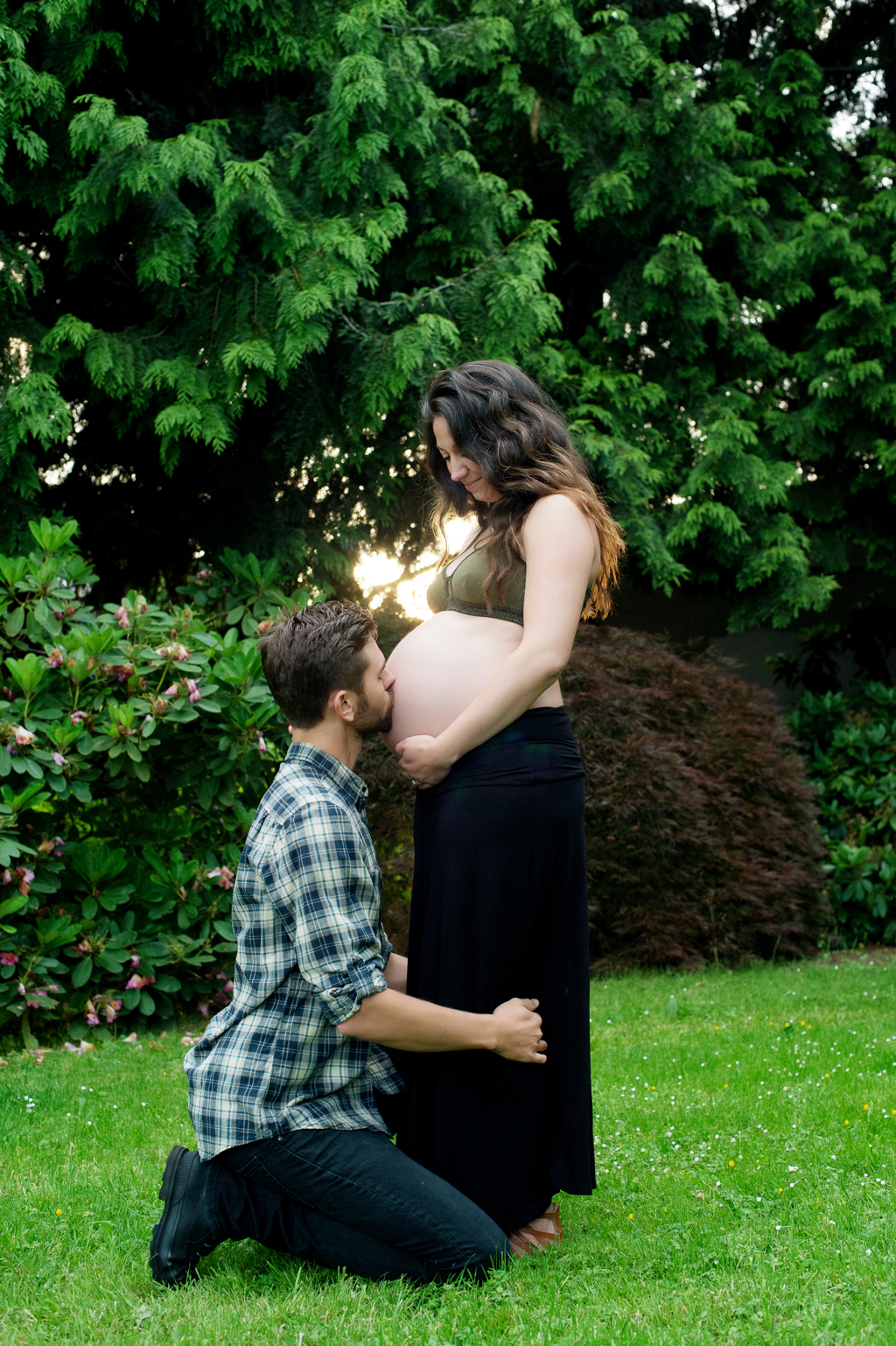 pregnant woman in forest green bralette  looks down at belly as husband kisses the belly