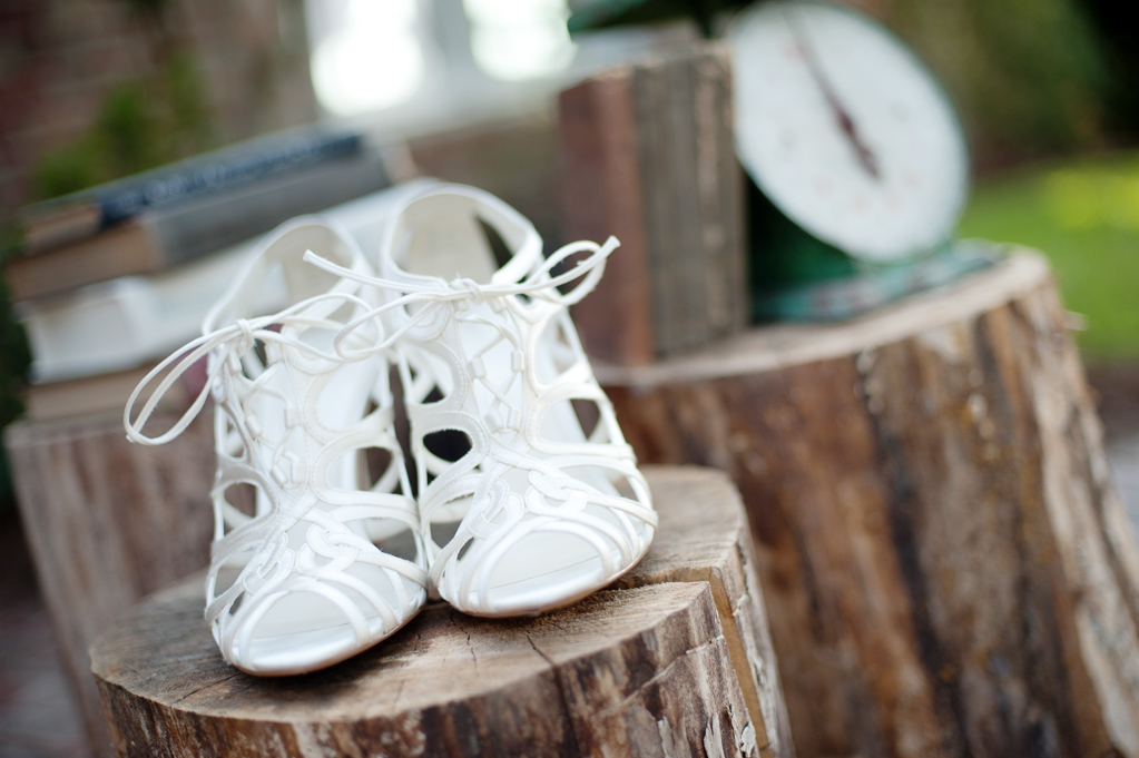 the brides strappy white wedding day heels sit on a stump