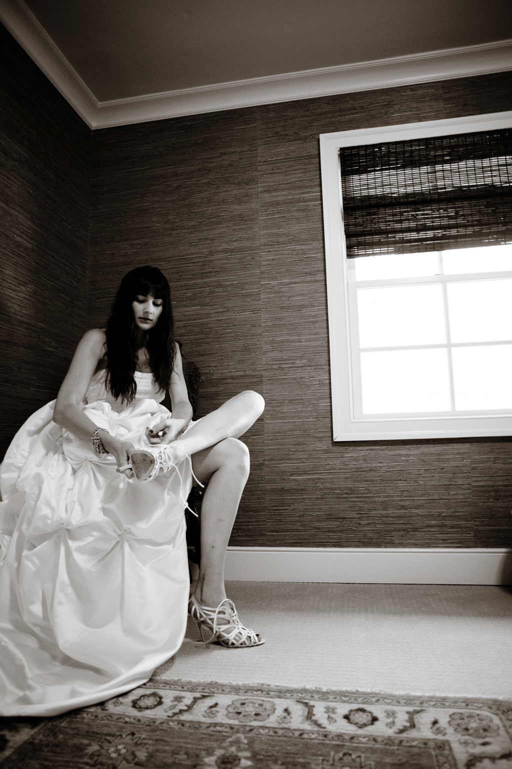 the bride sits in a corner of a room putting on her shoes
