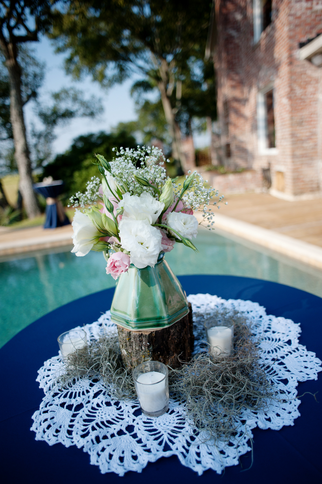 pretty green vase filled with white and pink flowers on a cocktail table covered in navy tablecloth, lace and spanish moss