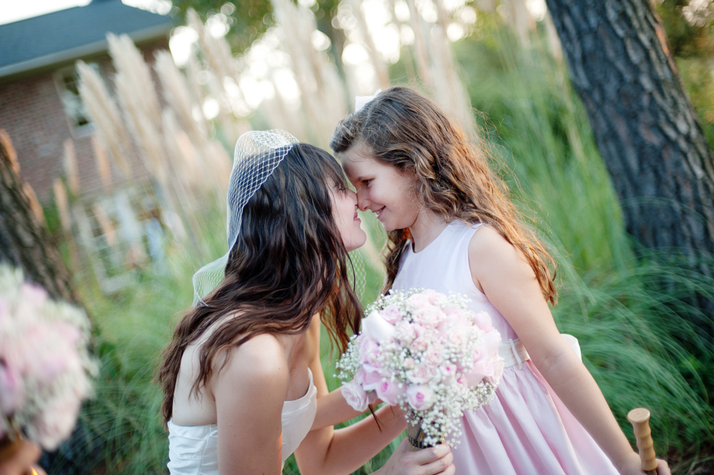a bride kneels down to touch noses with a flower girl