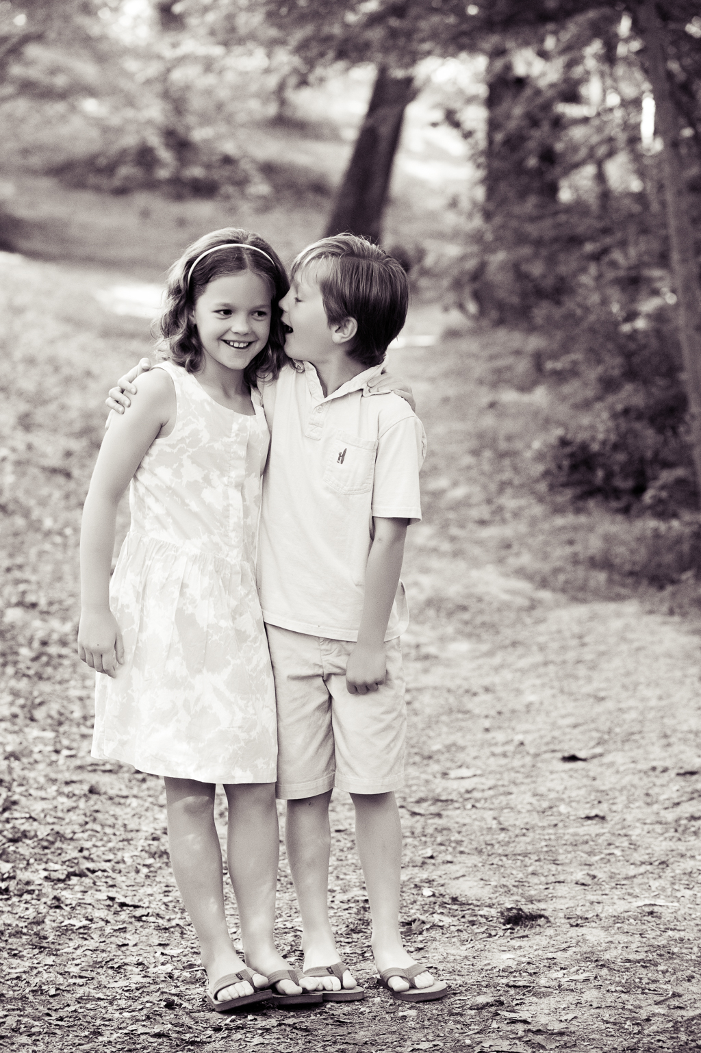 a little boy whispers something in his sisters ear