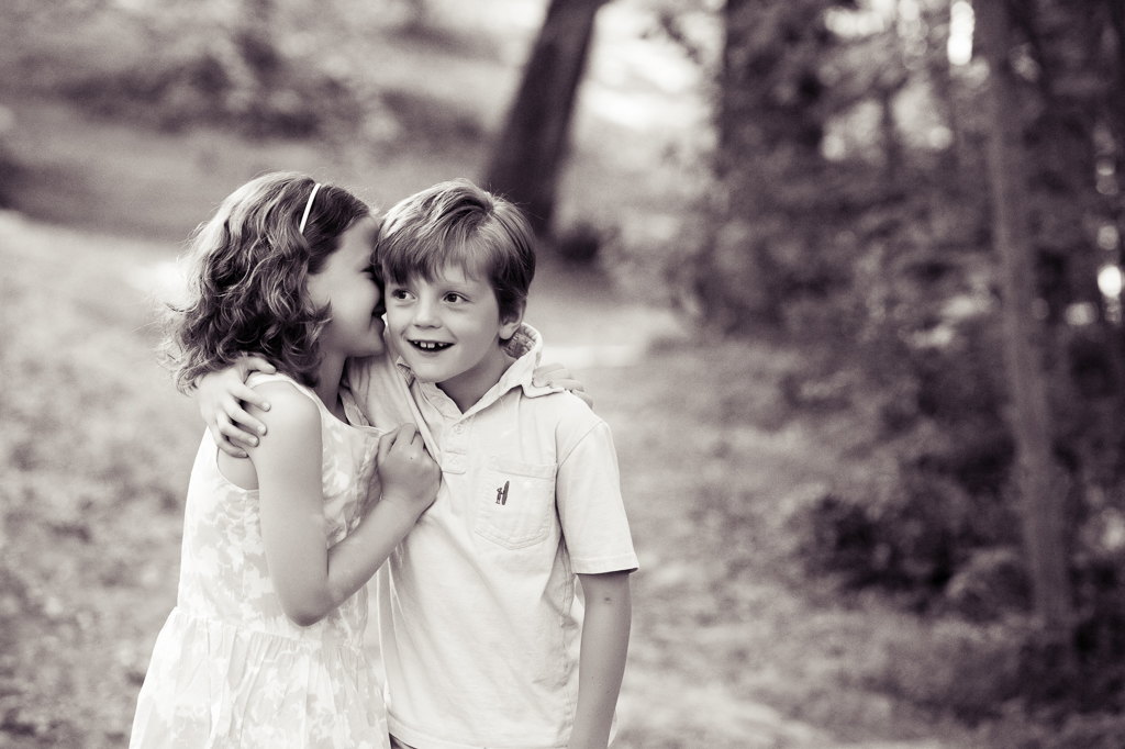 a little girl whispers a secret in her brother's ear