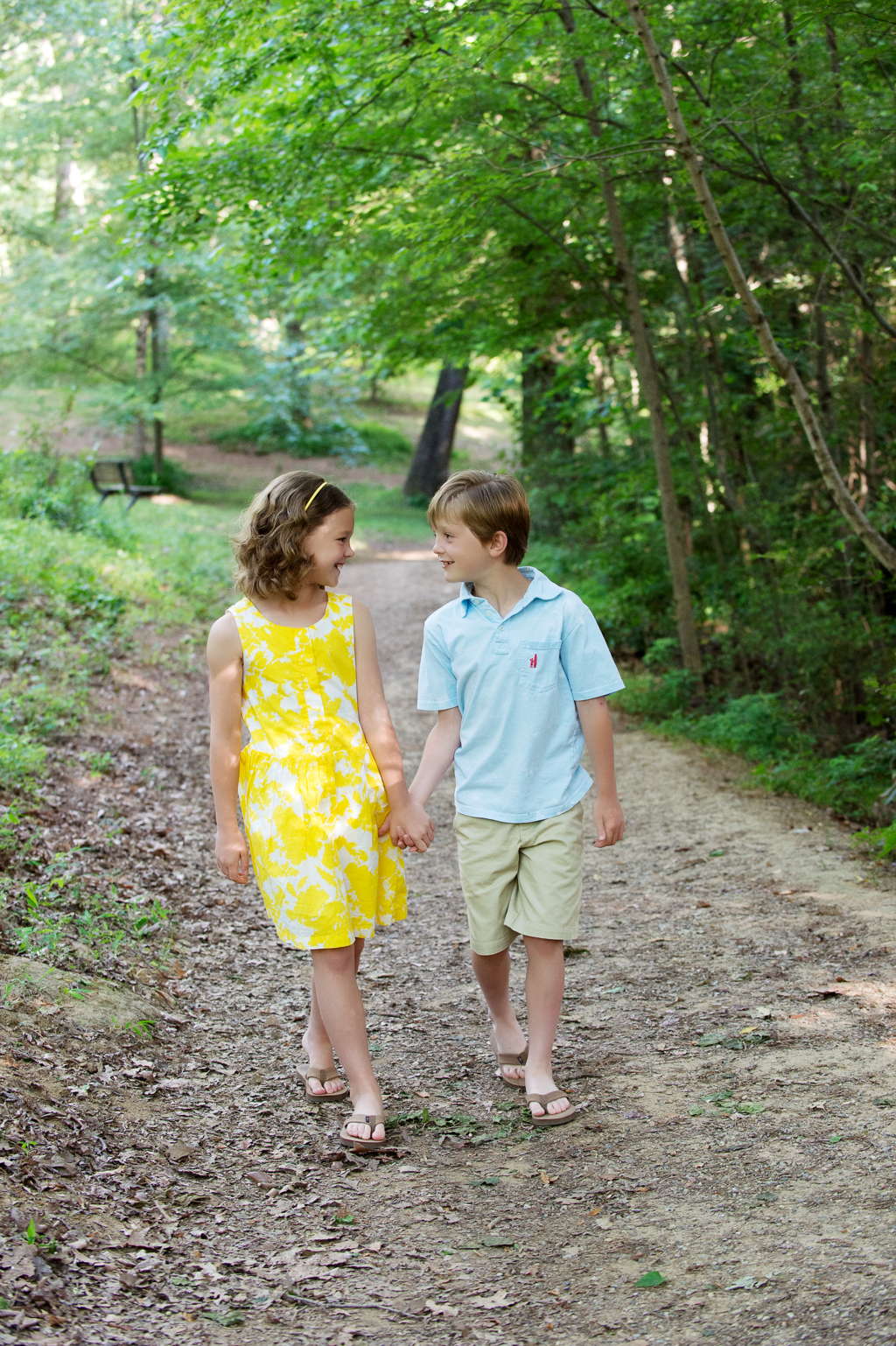 a brother and sister hold hands as they walk down a trail in the woods at latta park