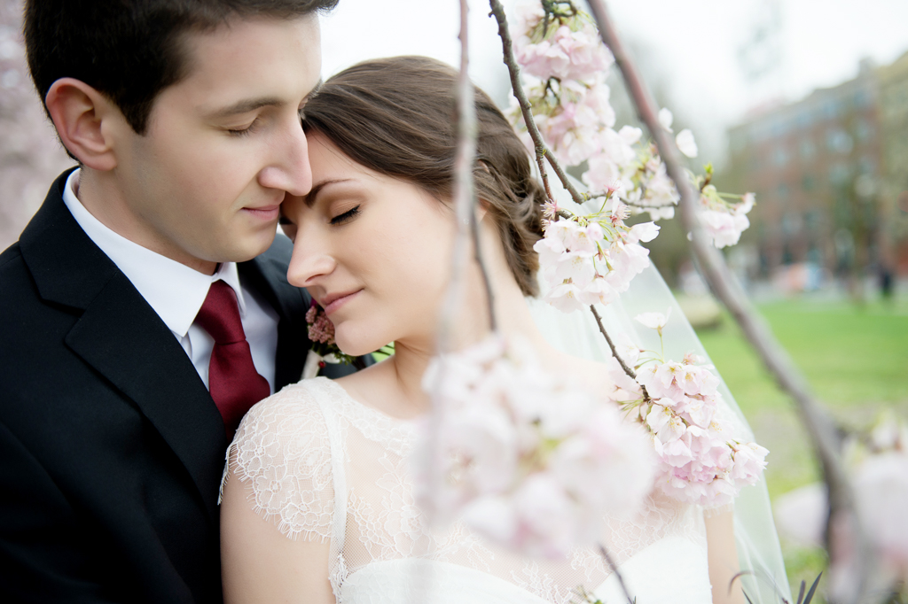 a bride and groom lean their heads together underneath a cherry blossom tree