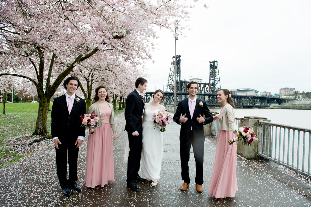 bridesmaids in pink dresses and groomsmen walk with the bride and groom along the portland riverfront with cherry blossom trees blooming