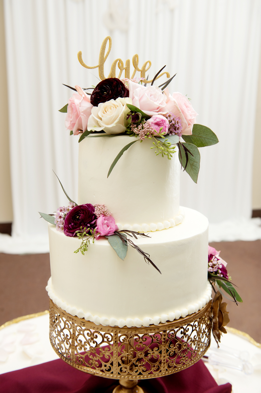 a pretty white wedding cake with pink and maroon flowers