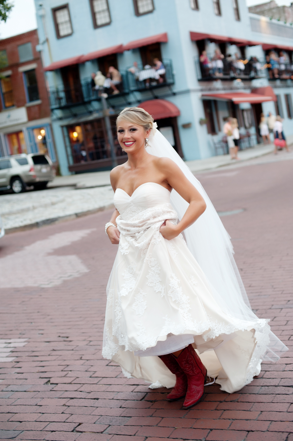 bride in red cowboy boots walks along a cobblestone road in front of roys riverboat landing