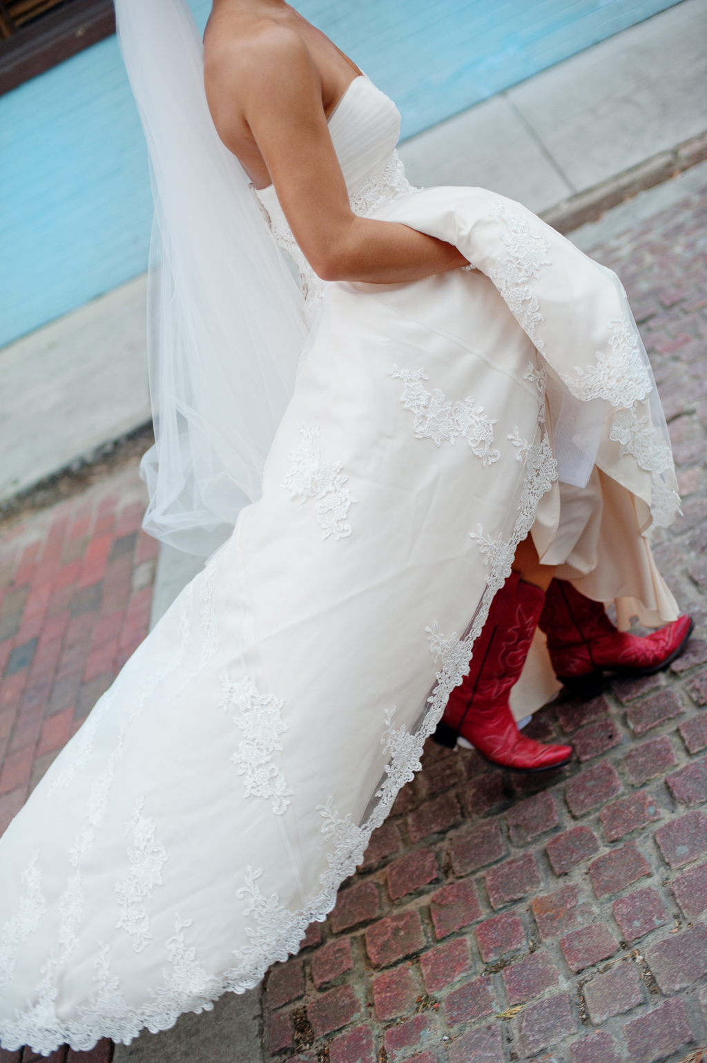 bride in red cowboy boots walks along a cobblestone road