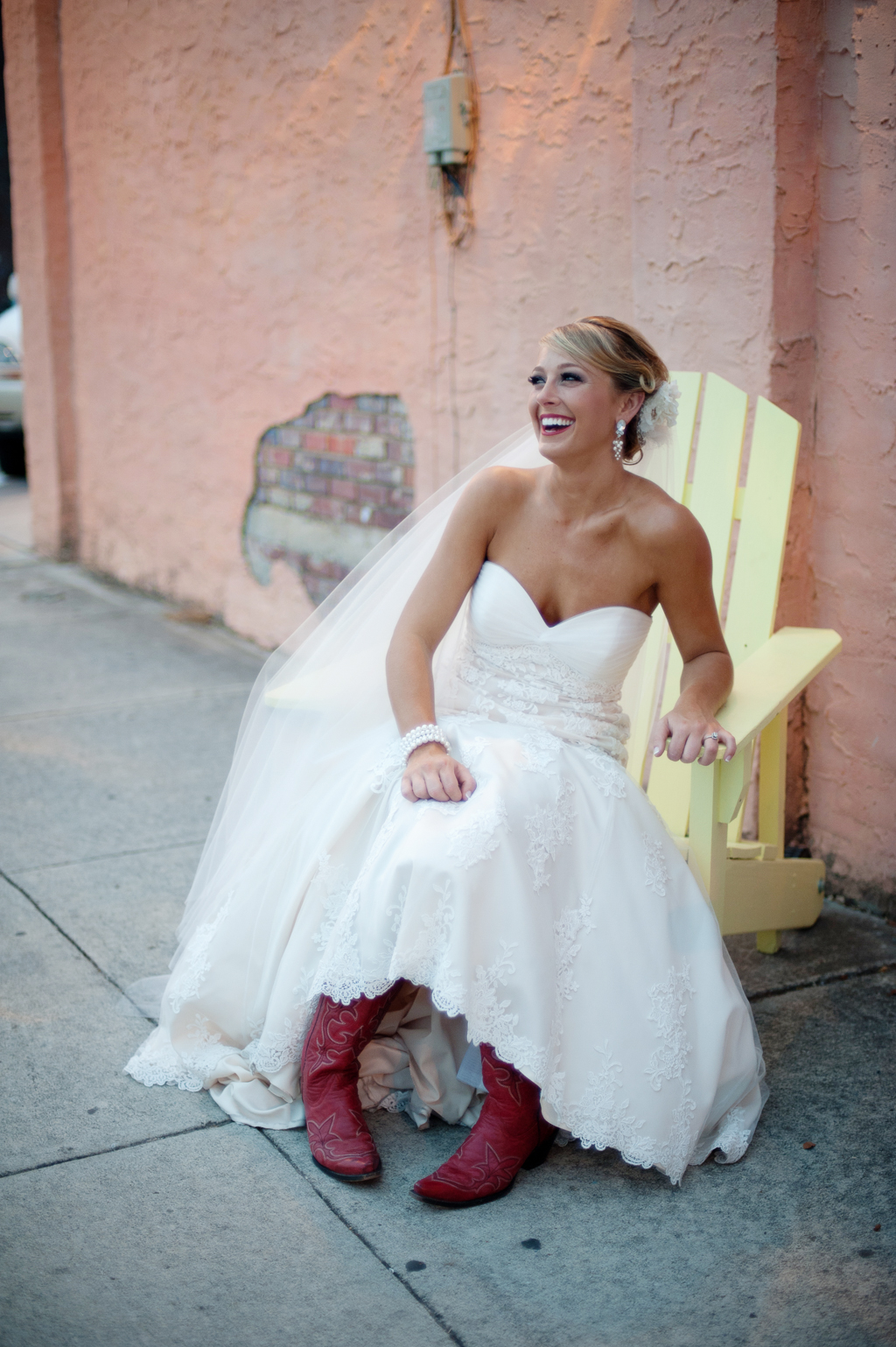 a bride in red cowboy boots sits in a yellow adirondack chair