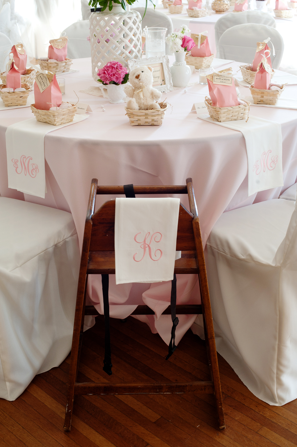 a white and pink monogrammed embroidered napkin over the back of a high chair at a wedding reception
