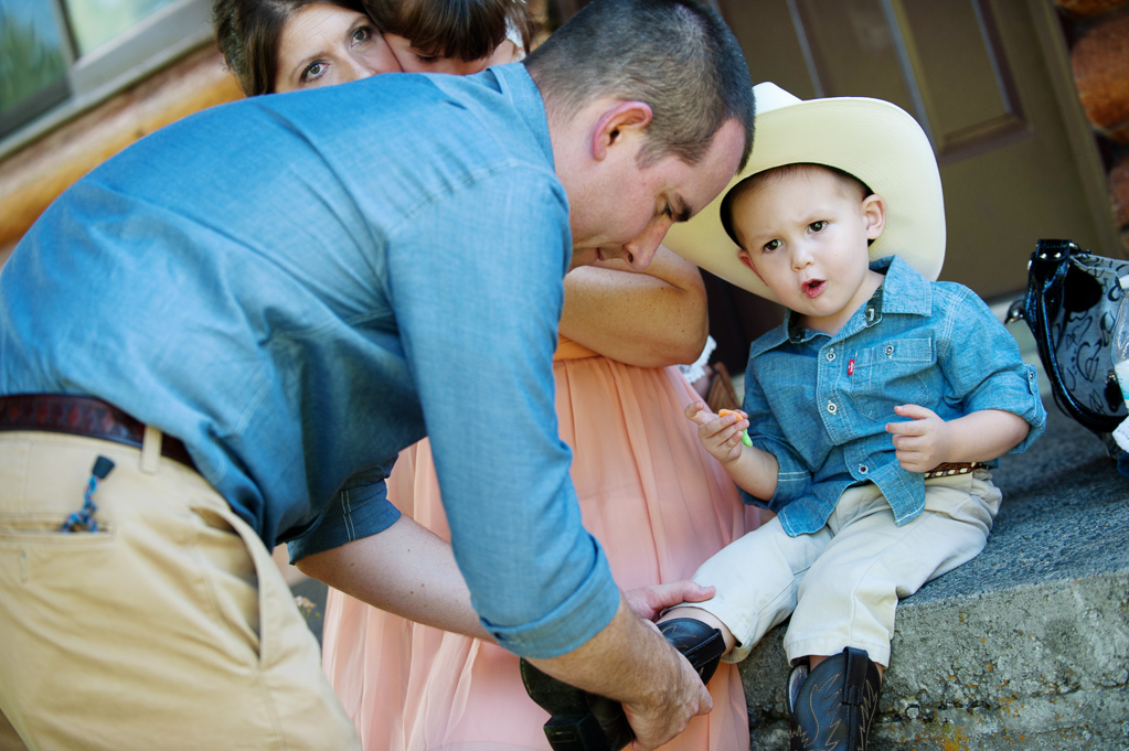 a man helps put cowboy boots on a young boy wearing a cowboy hat