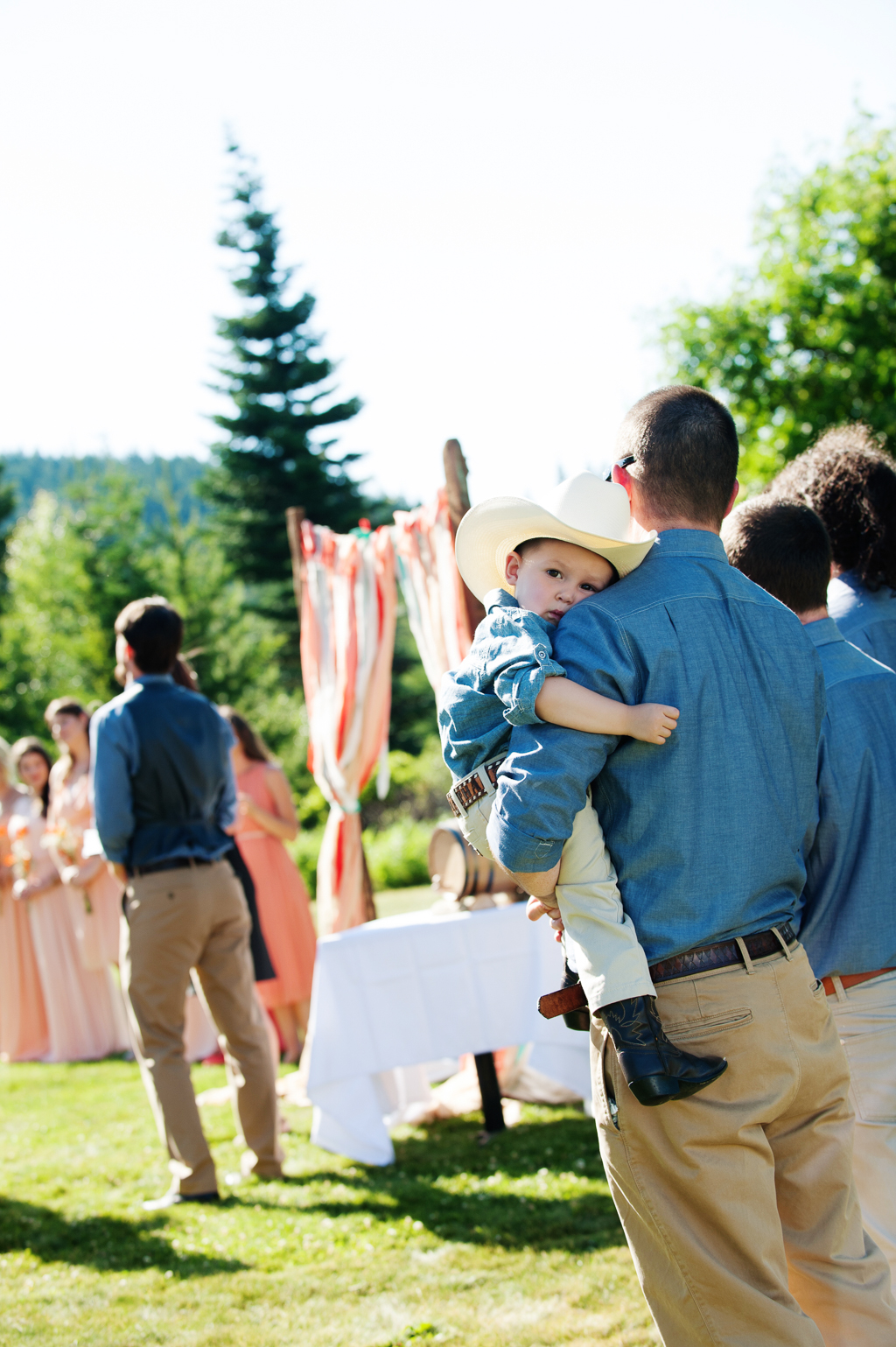 a groomsman holds a little boy wearing a cowboy hat and boots during a wedding ceremony