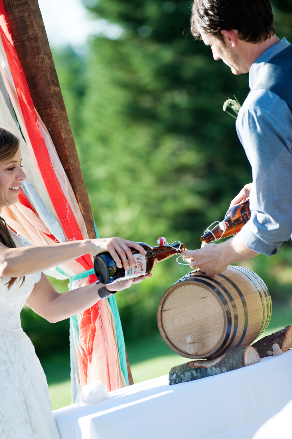 the bride and groom pour bottles of alcohol into a barrel during the wedding ceremony