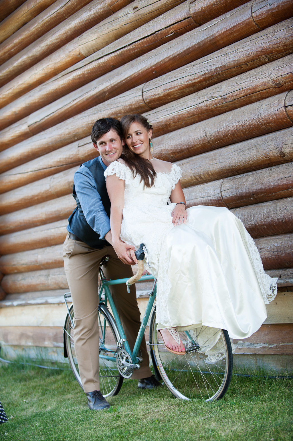 a bride sits on bike handlebars while her groom sits behind her