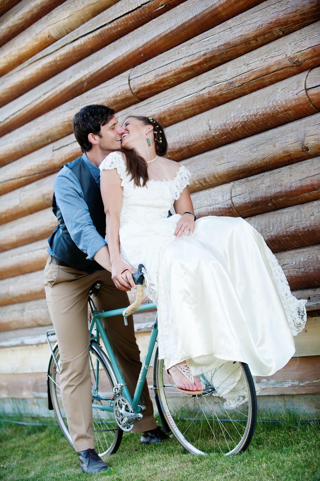 a bride sits on bike handlebars and gives her groom a kiss