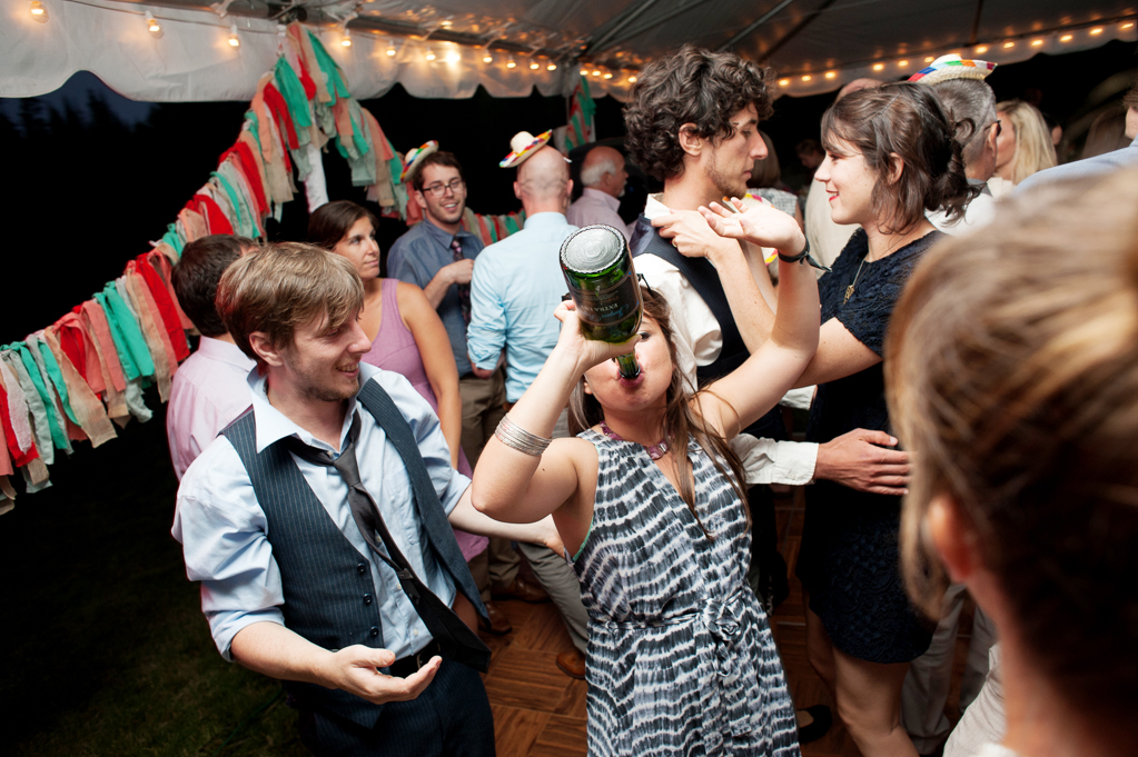 a woman drinks from a large alcohol bottle on the dance floor at a wedding reception