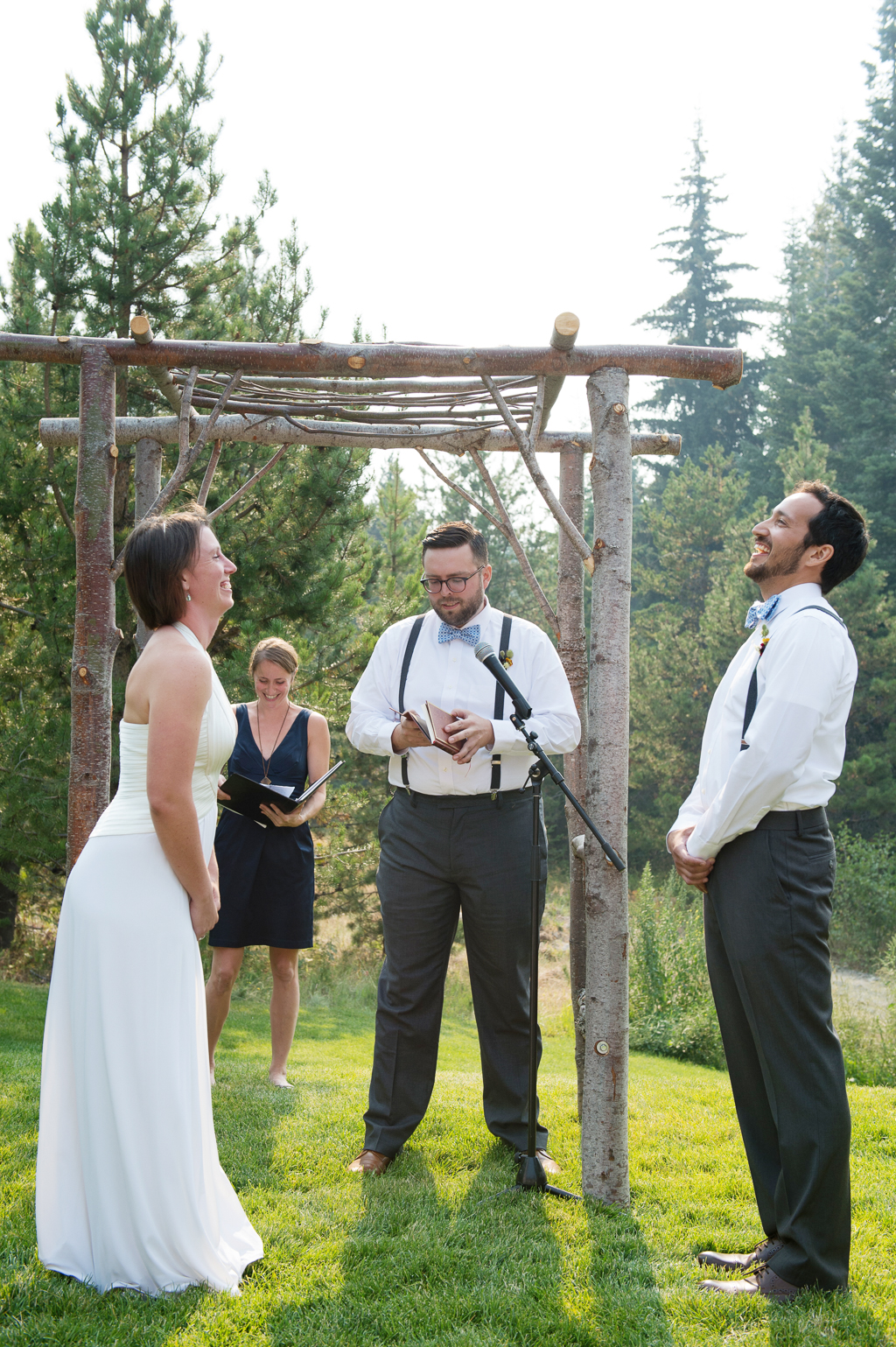 a bride and groom laugh during their vows in front of a wedding arbor made of logs
