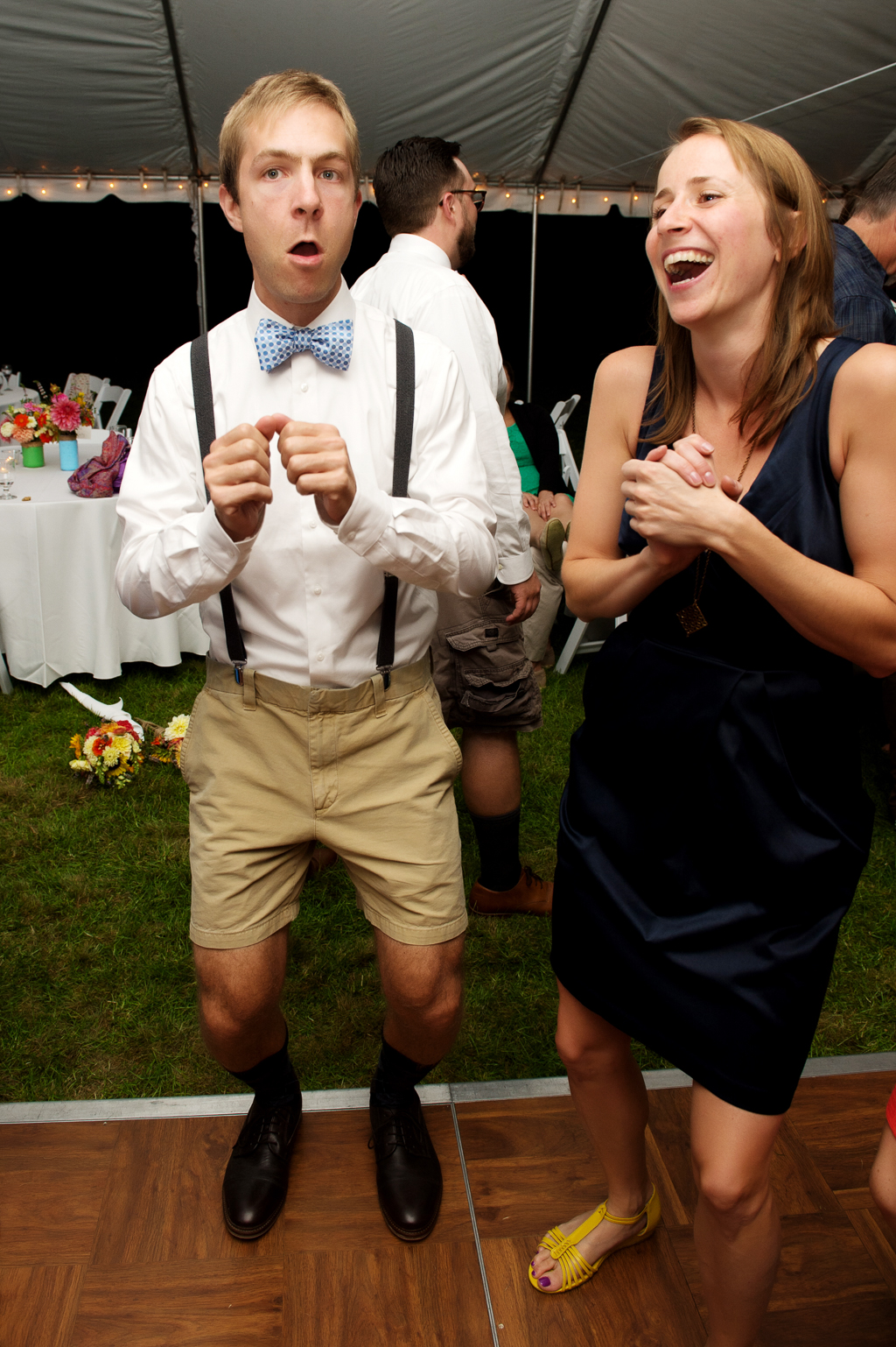 a groomsman dressed in lederhosen makes a girl laugh at the wedding reception