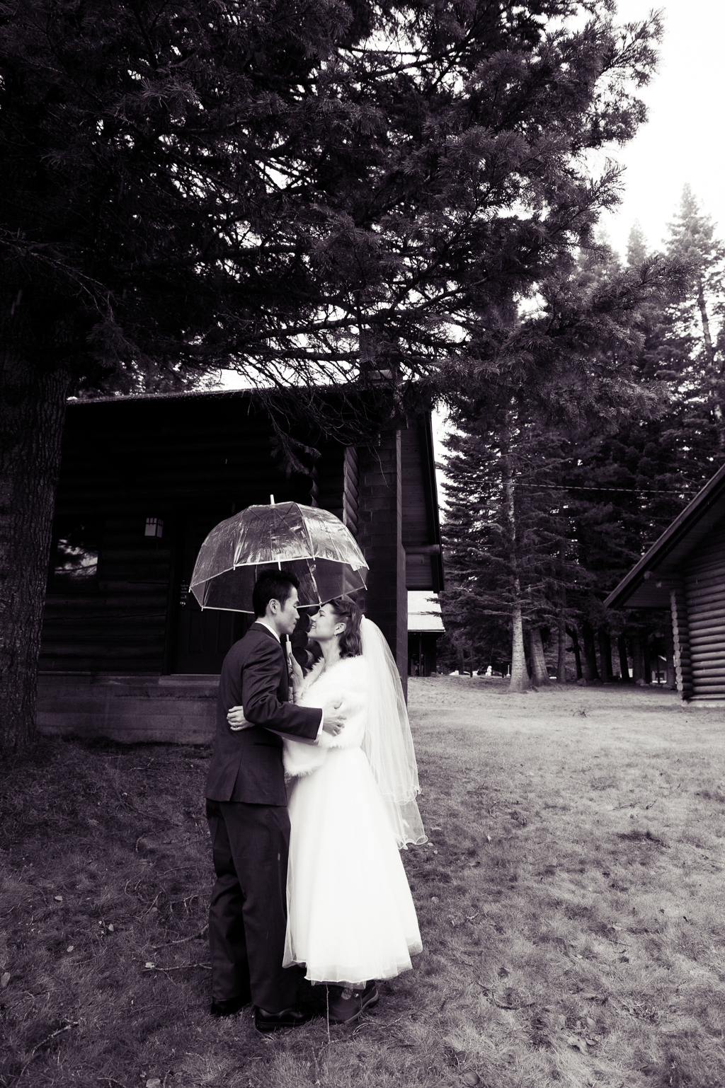 bride and groom share a moment under a clear umbrella in the rain