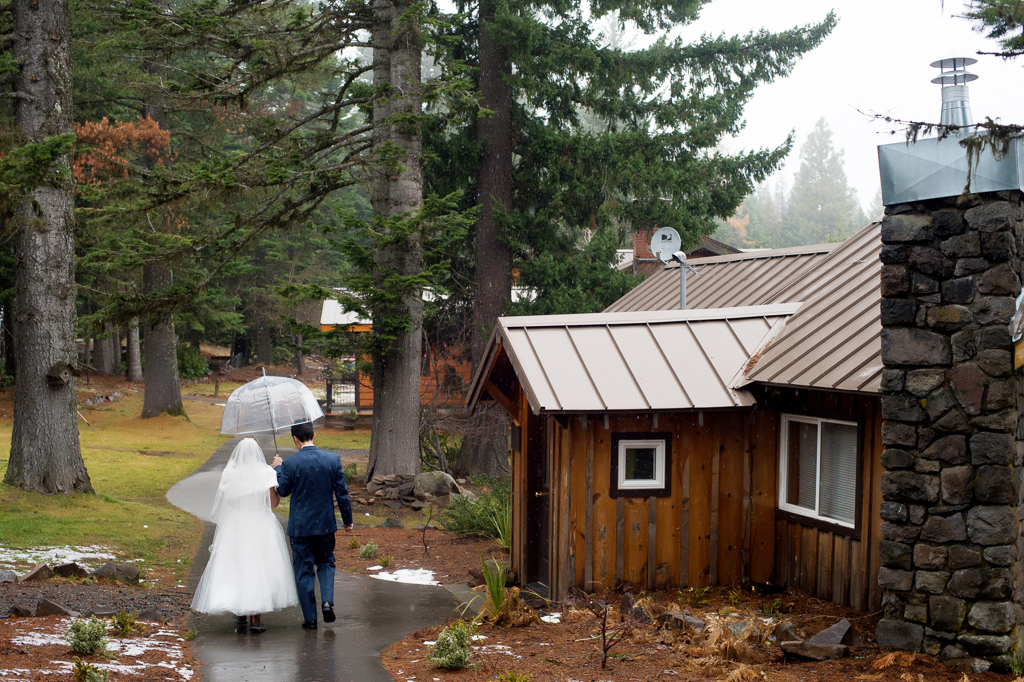 bride and groom walk down a path in the rain holding a clear umbrella