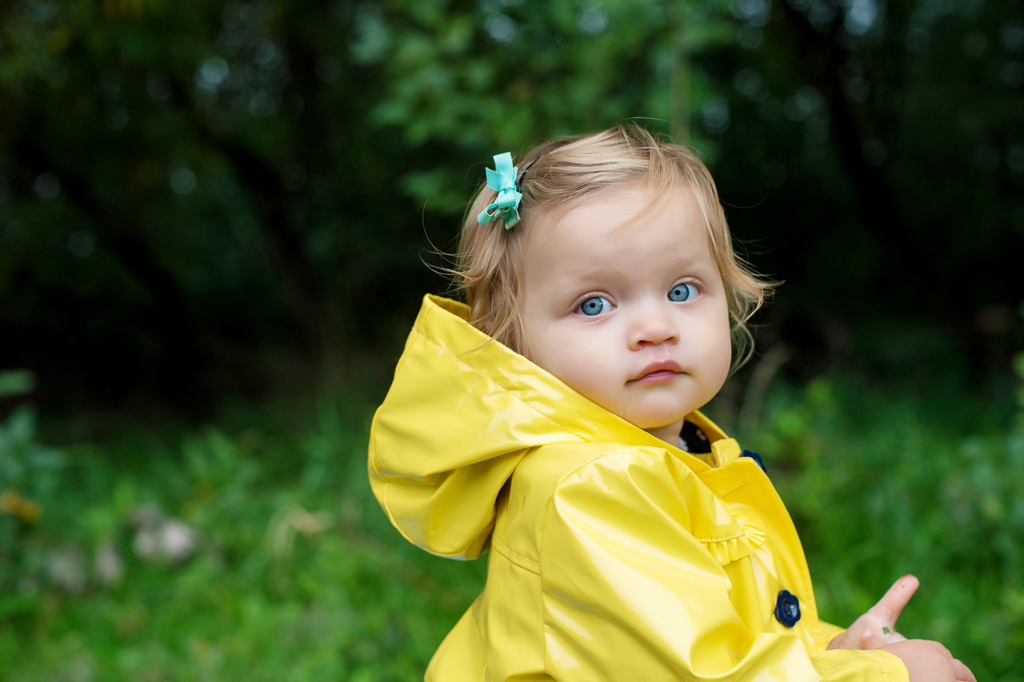 a little girl with bright blue eyes wears a vibrant yellow raincoat 