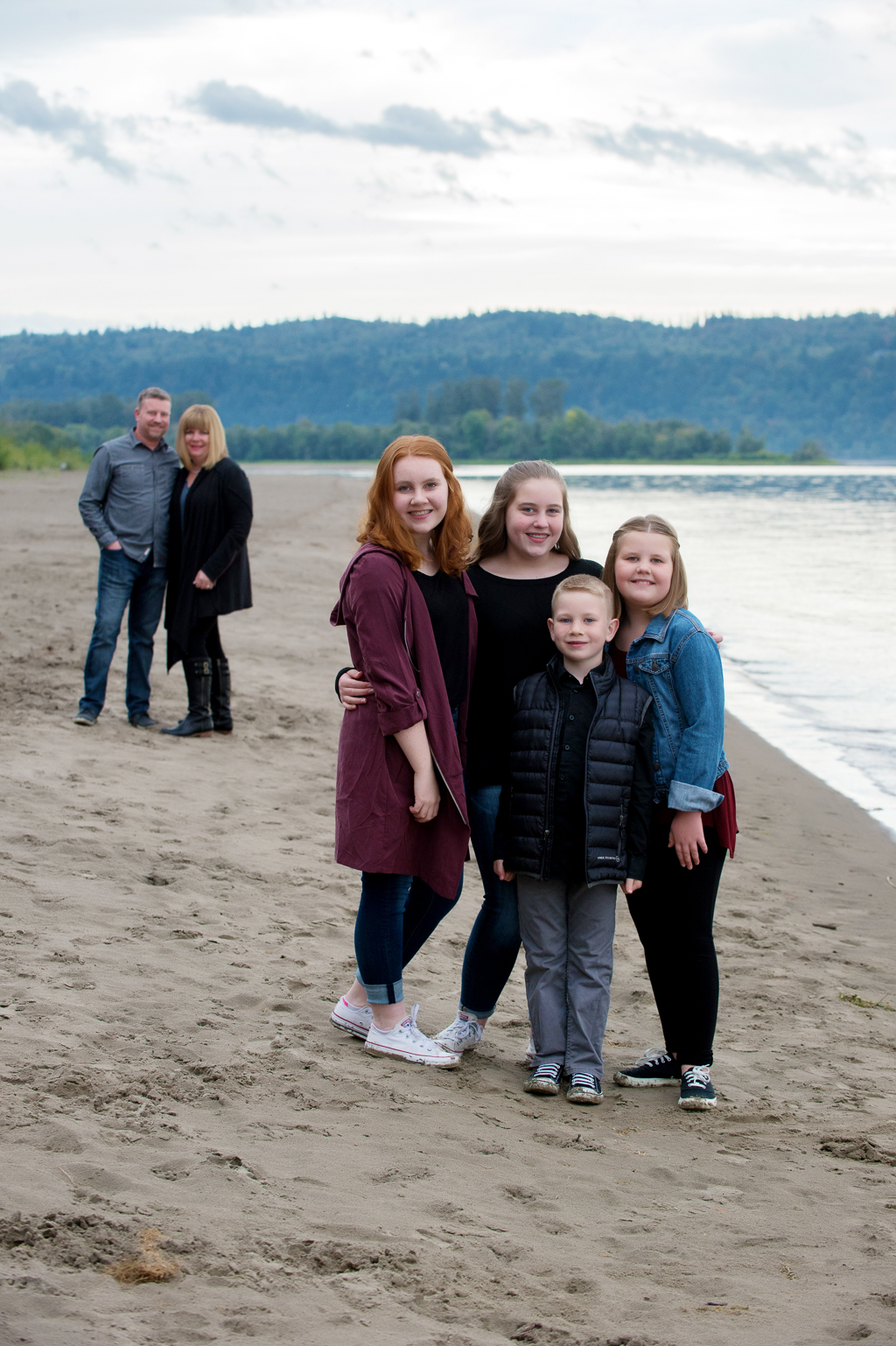 4 siblings hug together in the foreground while their parents hug in the background beside the columbia river