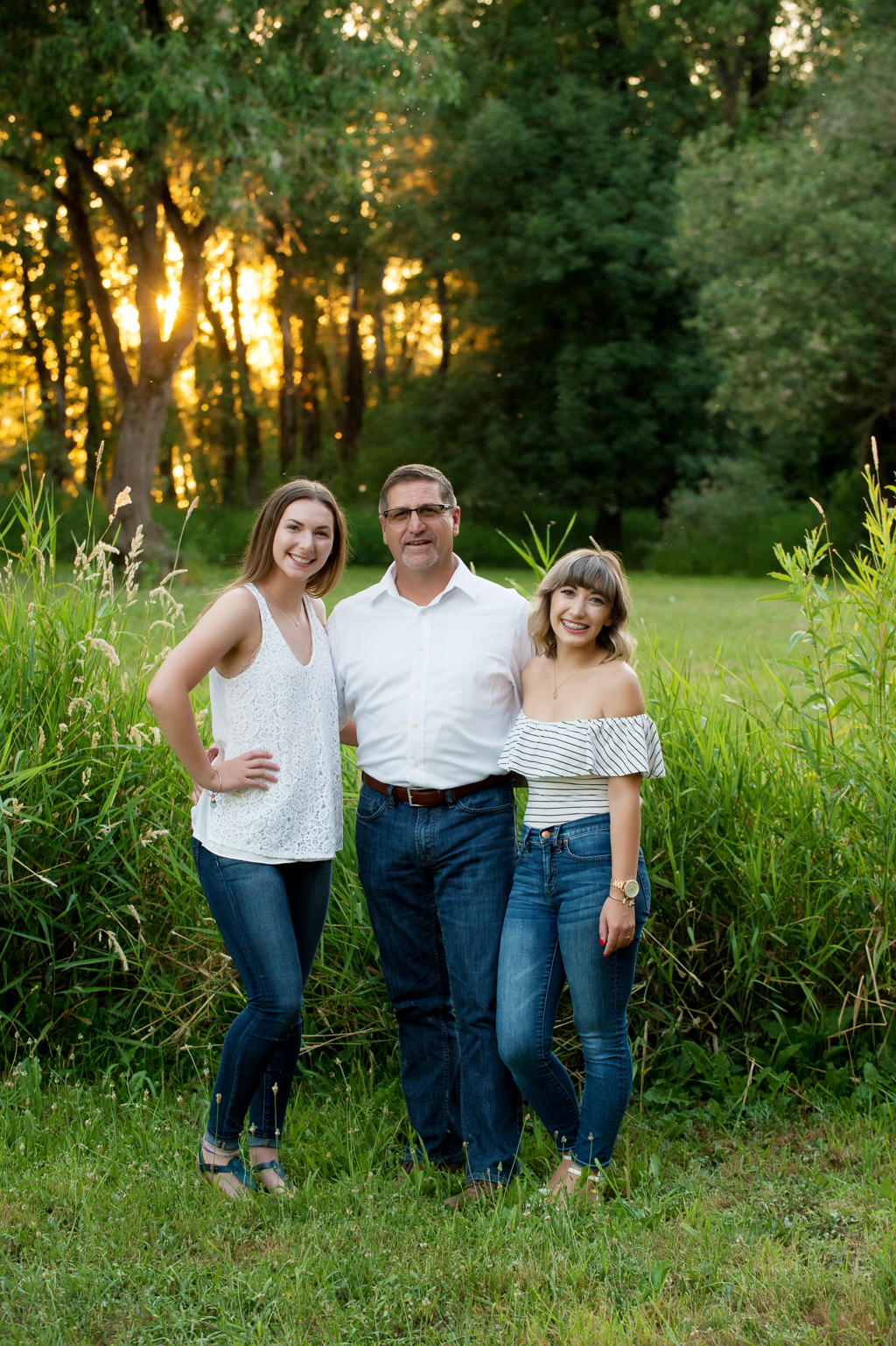 dad with his two daughters in front of trees and a golden sunset