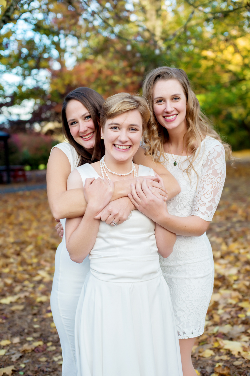 3 girls in white dresses hug in the autumn leaves