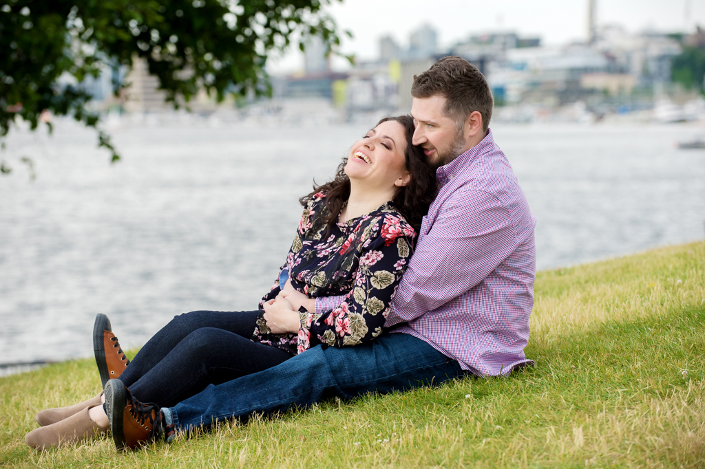 a couple sit and laugh in the grass at gasworks park overlooking the bay