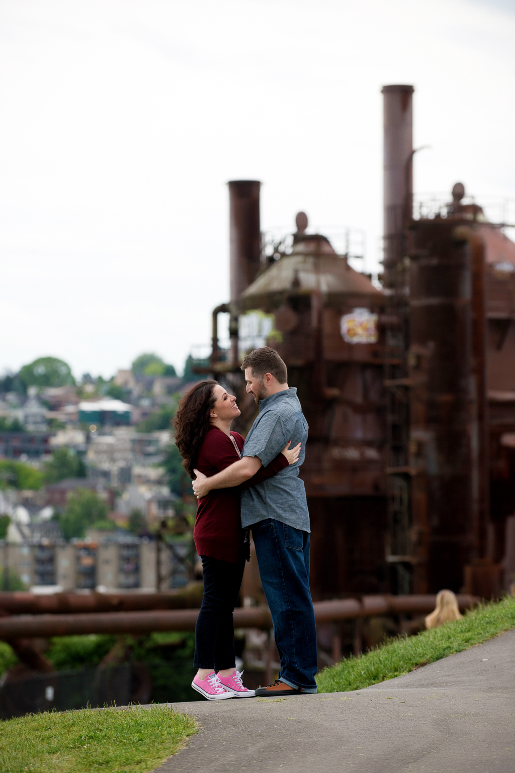 a couple embrace as factory at gas works park looms behind them