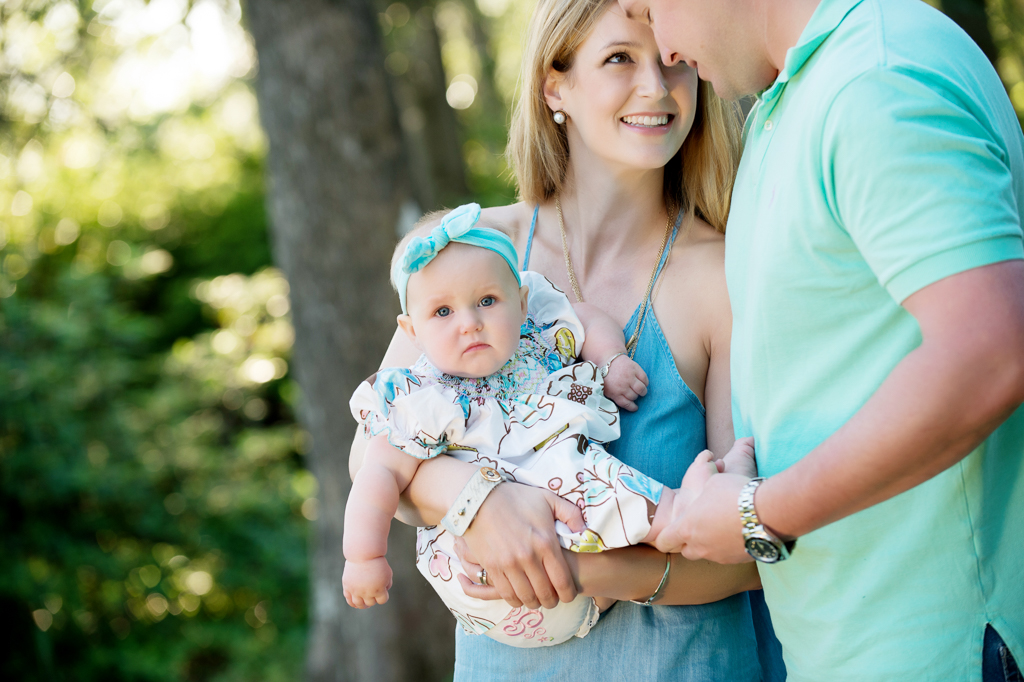 baby girl with big blue headband looks at camera as mom and dad look at each other