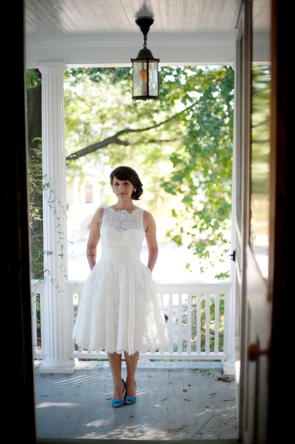 bride in tea length dress and blue shoes stands on porch