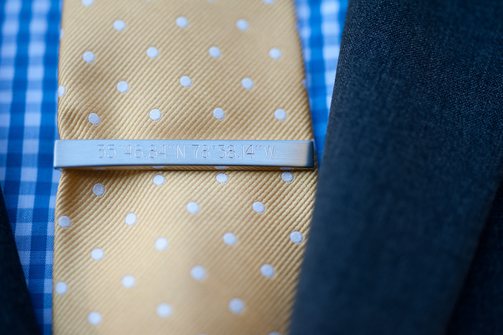 a blue plaid shirt with a yellow and white polka dot tie with a tie clip that has gps coordinates engraved