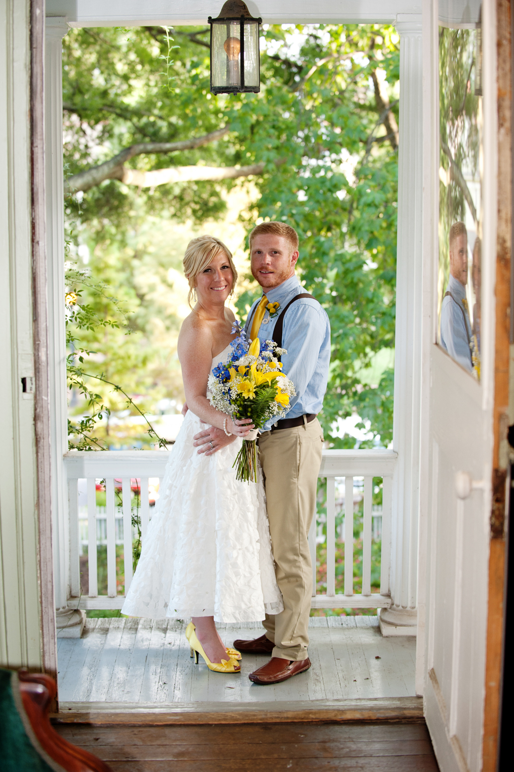 a bride and groom hug on the front porch of haywood hall wearing blue and yellow