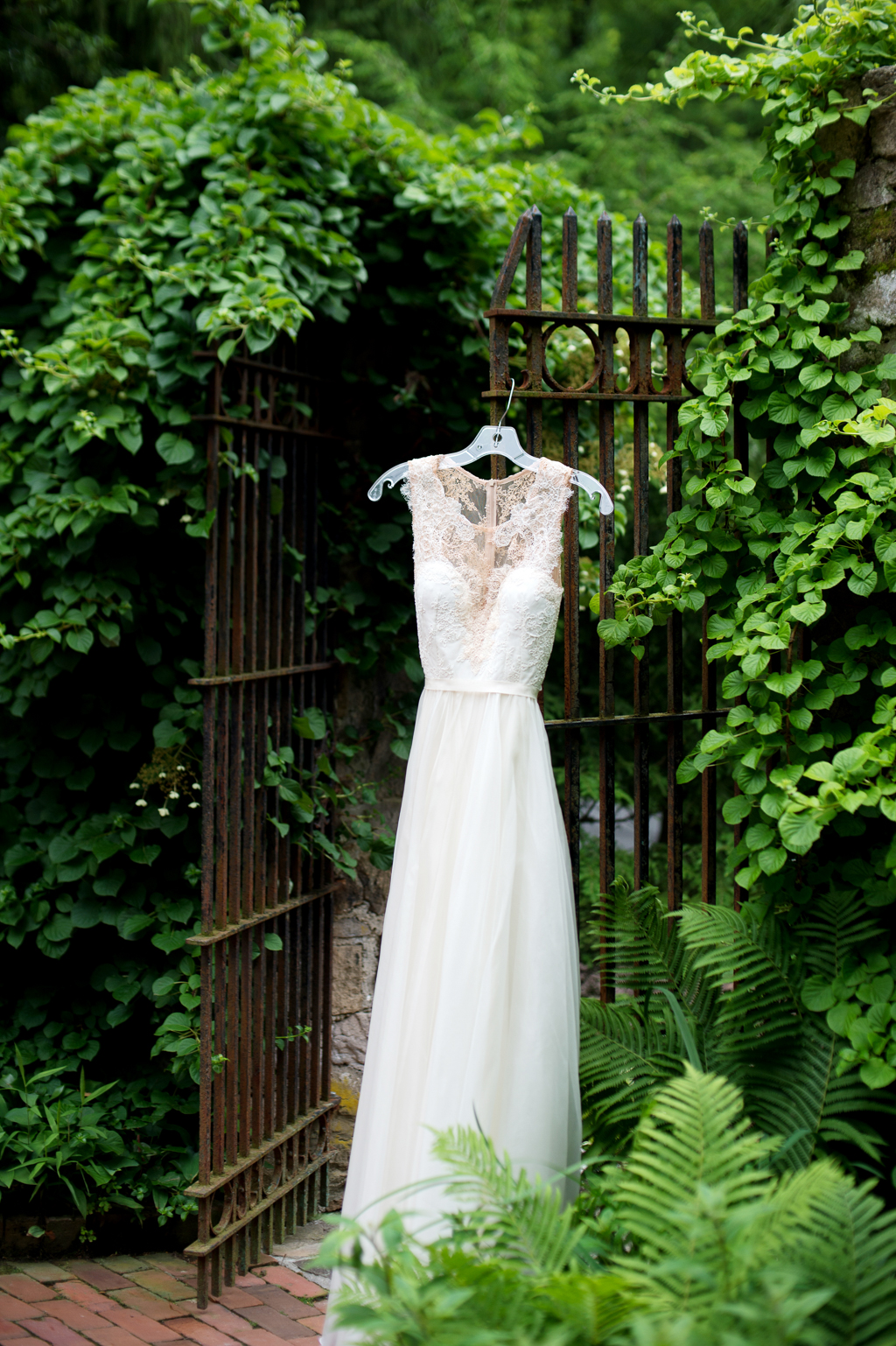 a wedding dress hangs from a wrought iron gate surrounded by ivy