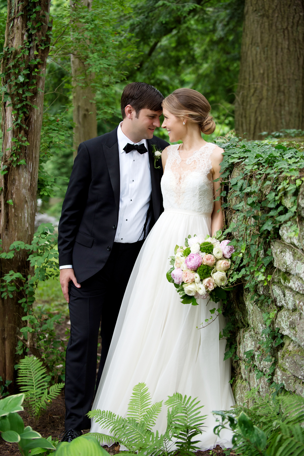 bride and groom lean against an ivy covered stone wall at holly hedge estate