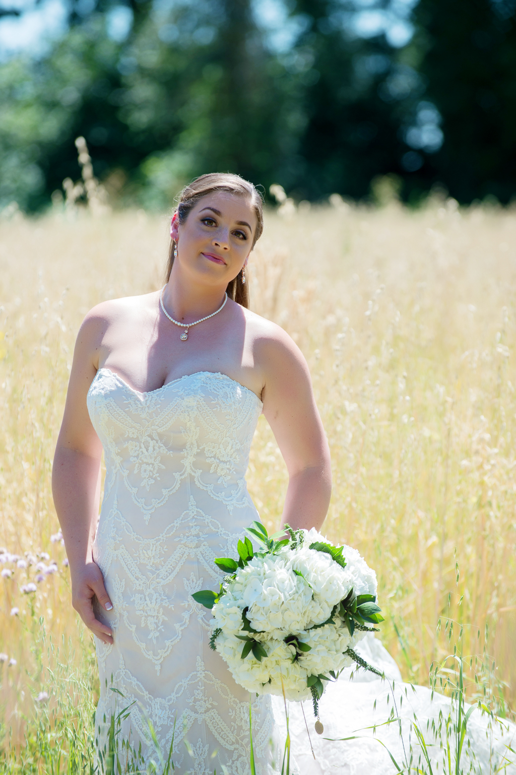 bride stands in a wheat field holding a white hydrangea bouquet