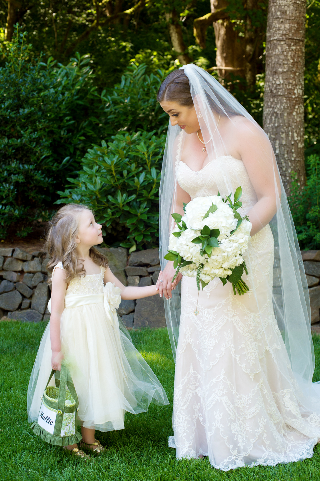 a bride holds a flower girl's hand as she looks up at her